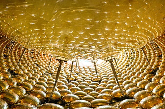 121624_ec_neutrino-detector_slide6 A large number of golden orbs surround part of an acrylic sphere.